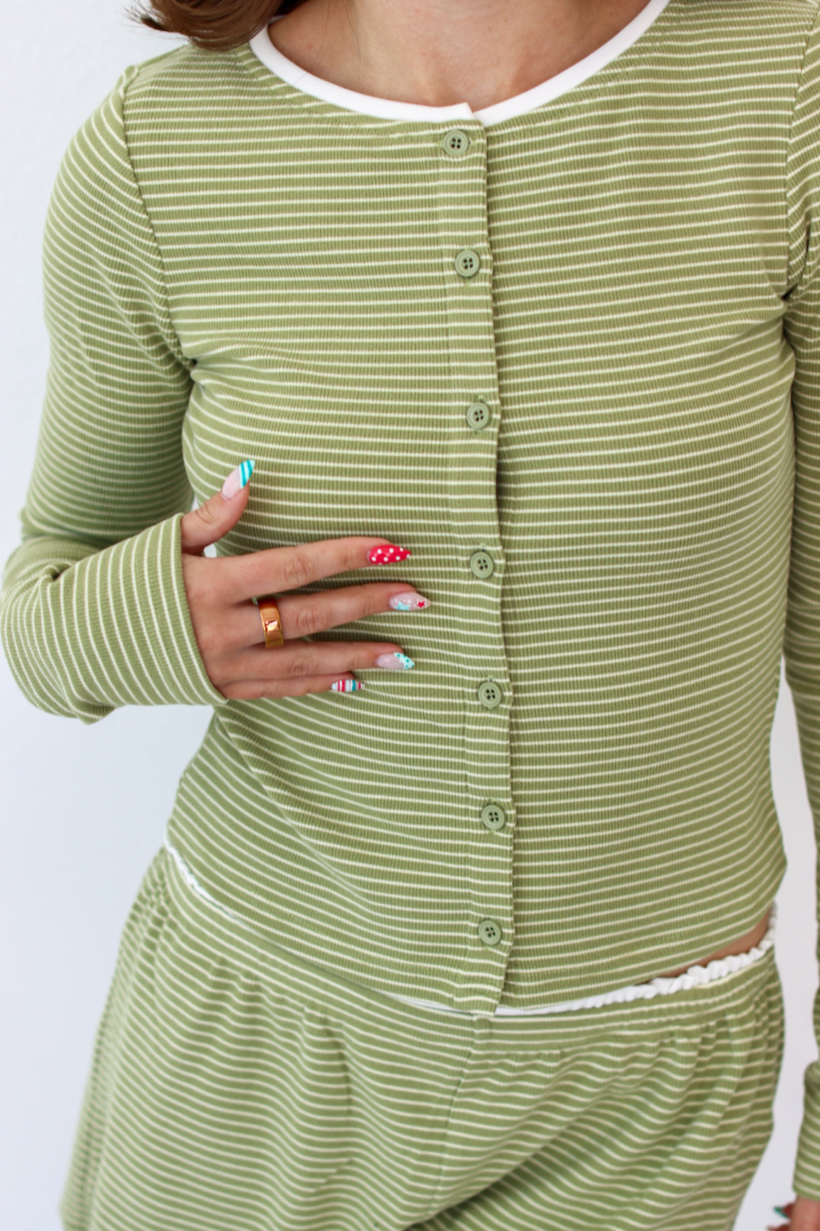 A close-up of a person wearing a light sage green and white striped long-sleeve button-front top and matching bottoms, with the hand resting on the chest.
