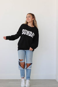 girl wearing black sweater with white "sunday" graphic