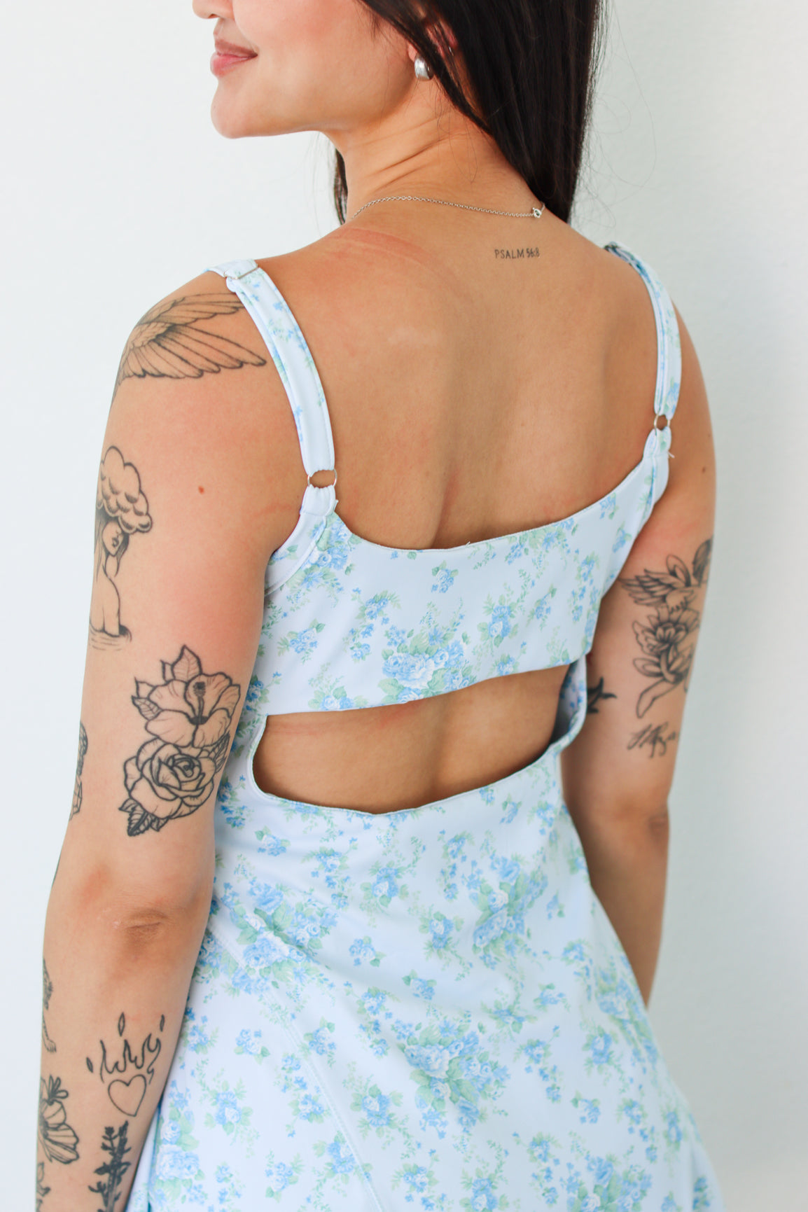 A woman shown from the back wearing a light blue and white floral cutout dress, featuring thin straps and a large open back design.
