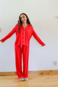 Woman wearing a red pajama set standing in a room with a white wall and wooden floor.