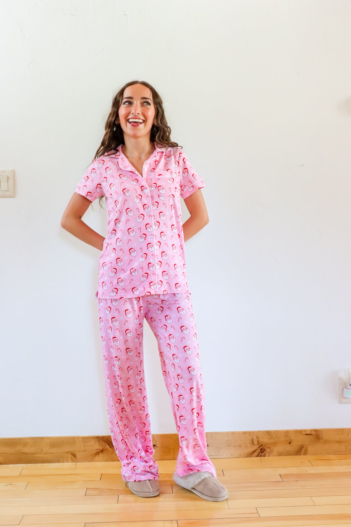 Woman wearing pink pajamas with a pattern, standing in a room with a wooden floor and white walls.