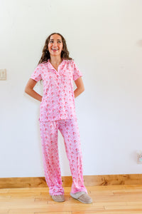 Woman wearing pink pajamas with a pattern, standing in a room with a wooden floor and white walls.