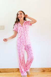 Woman wearing pink pajamas with a pattern, standing in a room with a white wall and wooden floor.
