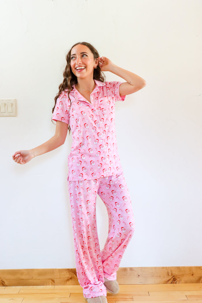Woman wearing pink pajamas with a pattern, standing in a room with a white wall and wooden floor.