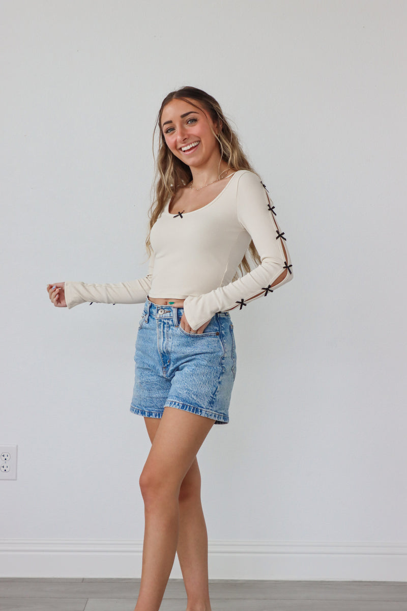 girl wearing cream long sleeve top with bow cutout details