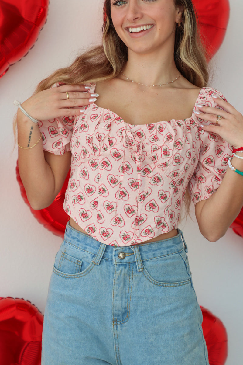 girl wearing light pink cropped top with puff sleeves and heart floral pattern