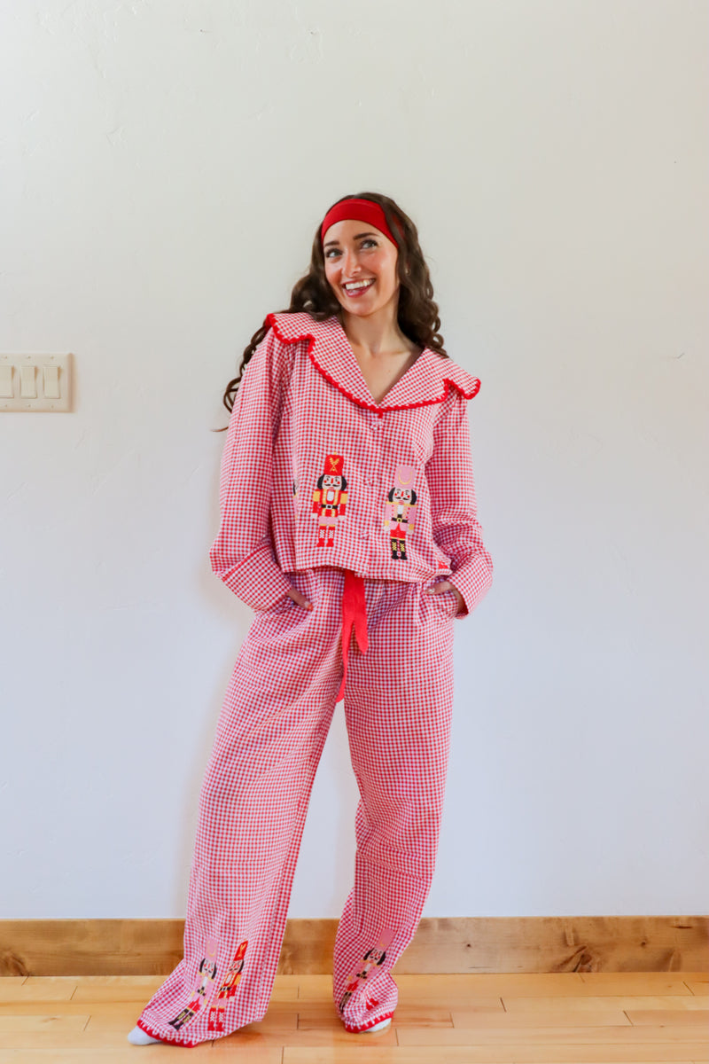 Woman wearing a red checkered pajama set with embroidered details against a white wall.