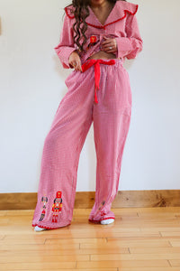 Person wearing a red checkered outfit with ruffled top and embroidered details on a wooden floor.