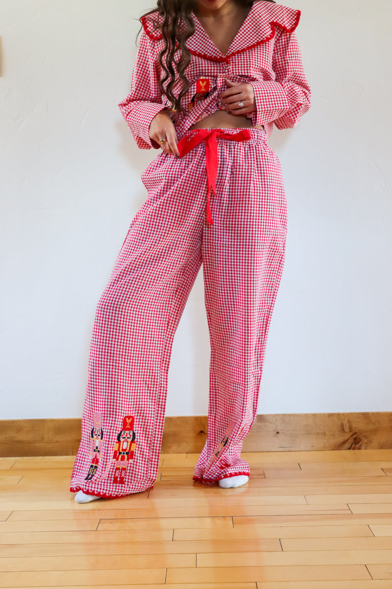 Person wearing a red checkered outfit with ruffled top and embroidered details on a wooden floor.