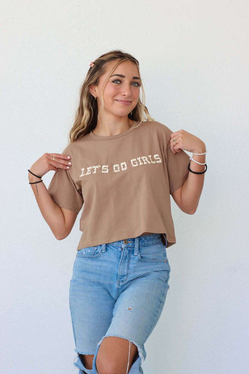 girl wearing brown "let's go girls" embroidered t-shirt