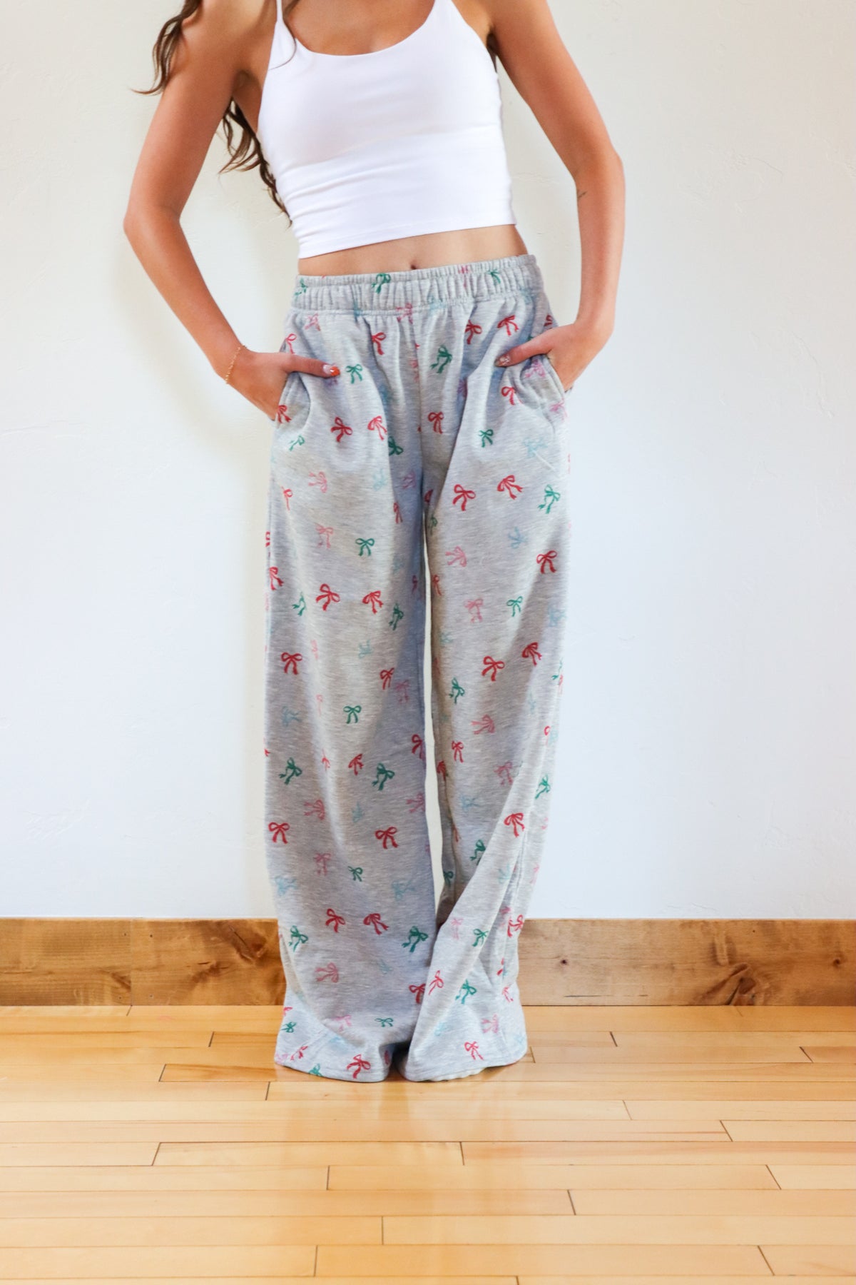 Person wearing light gray floral-patterned pants and a white top on a wooden floor.