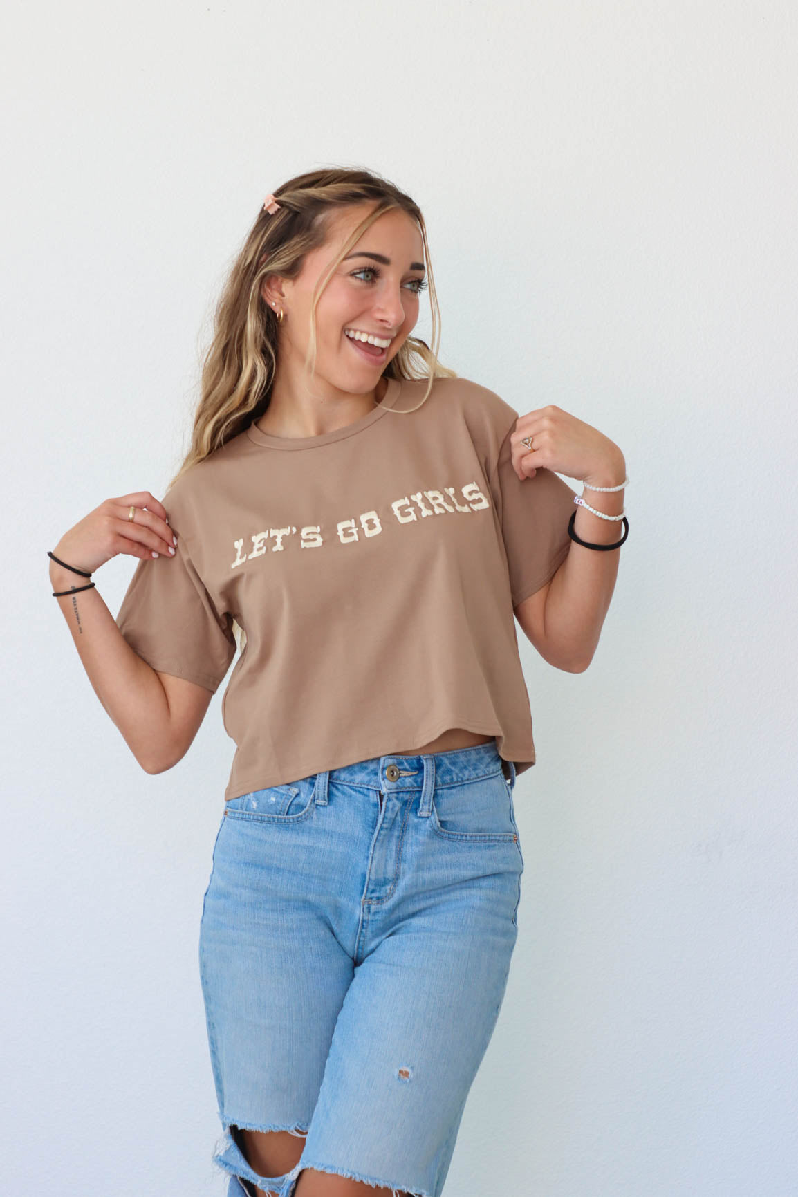 girl wearing brown "let's go girls" embroidered t-shirt