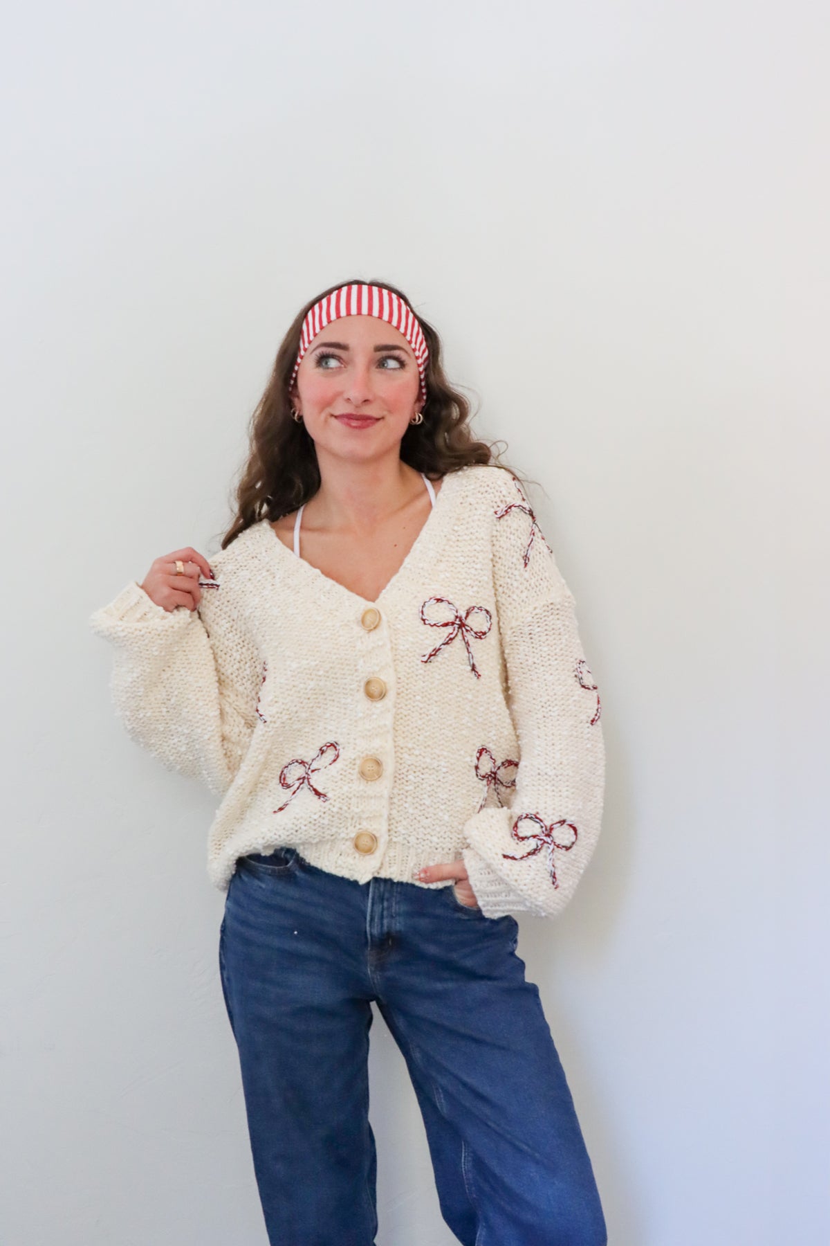 Woman wearing a cream cardigan with bow patterns against a white background
