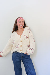 Woman wearing a cream cardigan with pink bow patterns against a white background