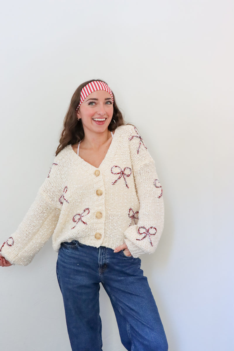 Woman wearing a cream cardigan with pink bow patterns against a white background