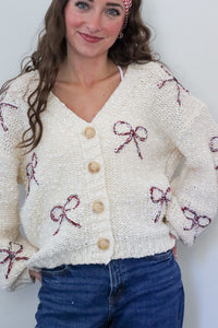 Woman wearing a cream cardigan with red bow patterns against a white background