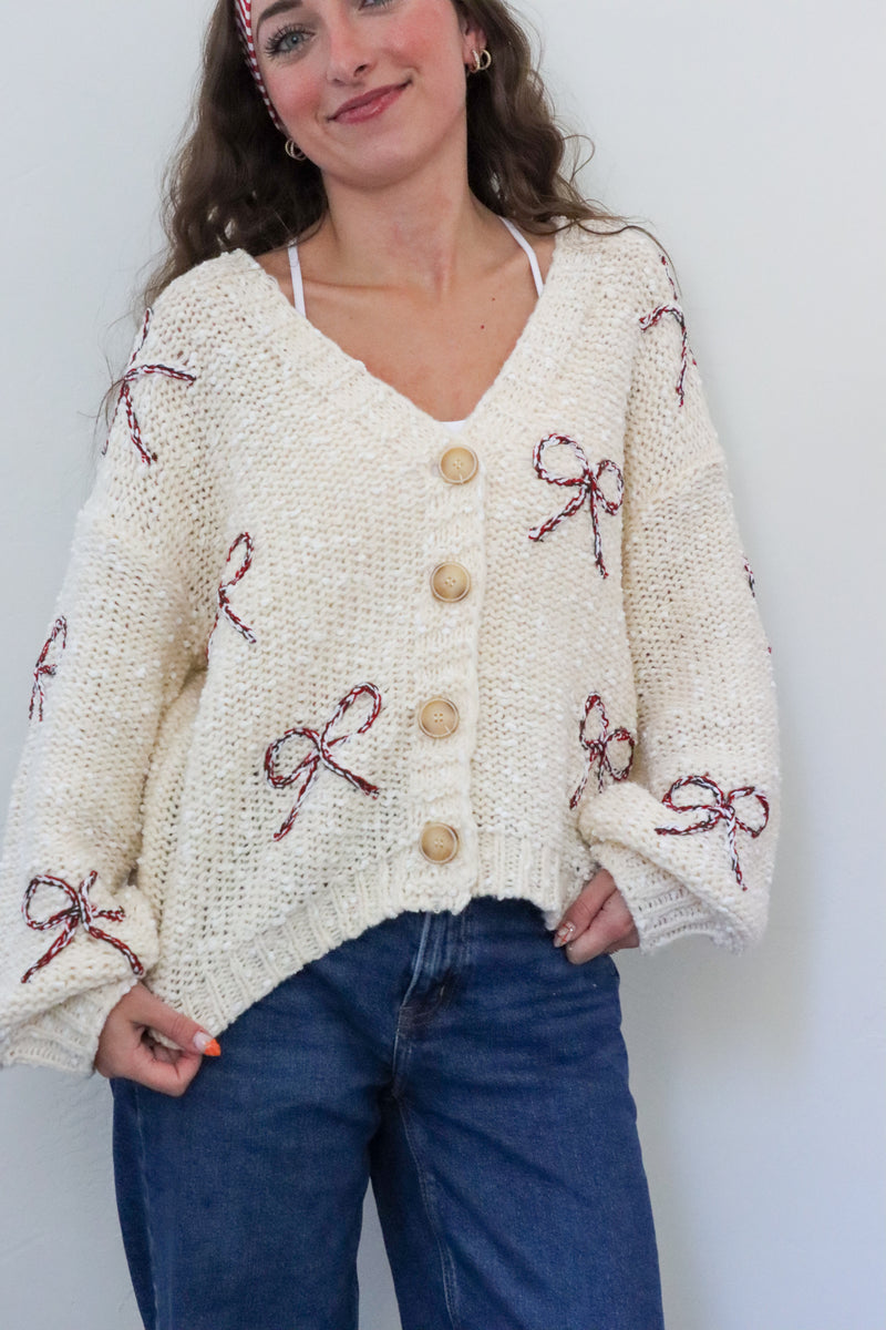 Woman wearing a cream cardigan with red bow patterns against a white background