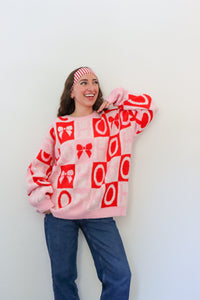 Person wearing a pink sweater with red patterns against a white background