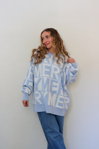 Person wearing a light blue sweater with text, standing against a plain background