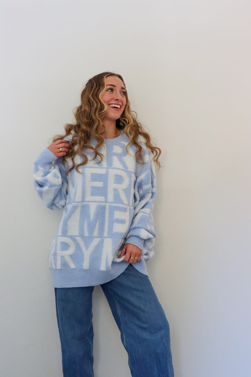 Woman wearing a light blue sweater with text standing against a white wall