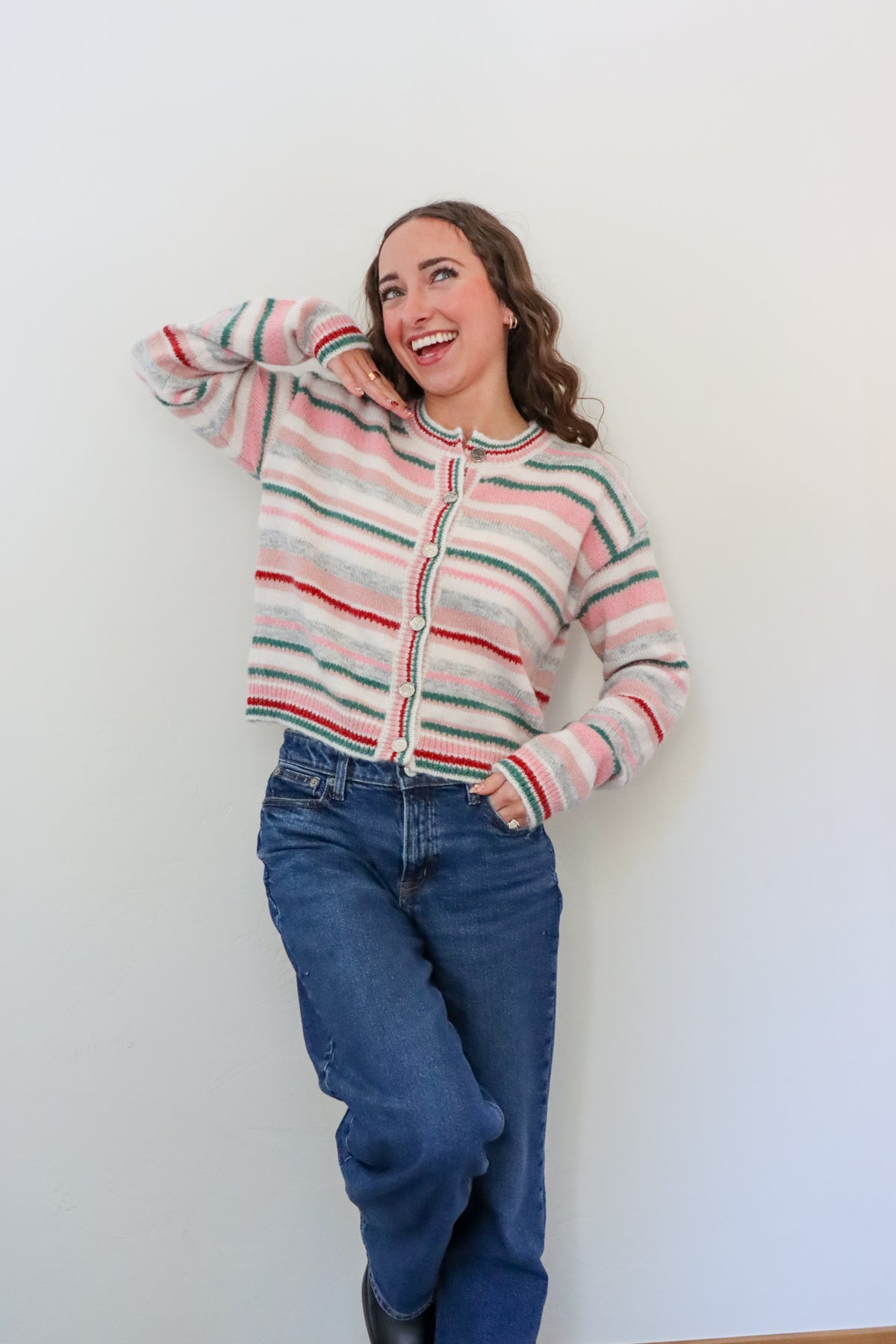 Woman wearing a striped sweater and blue jeans against a white wall