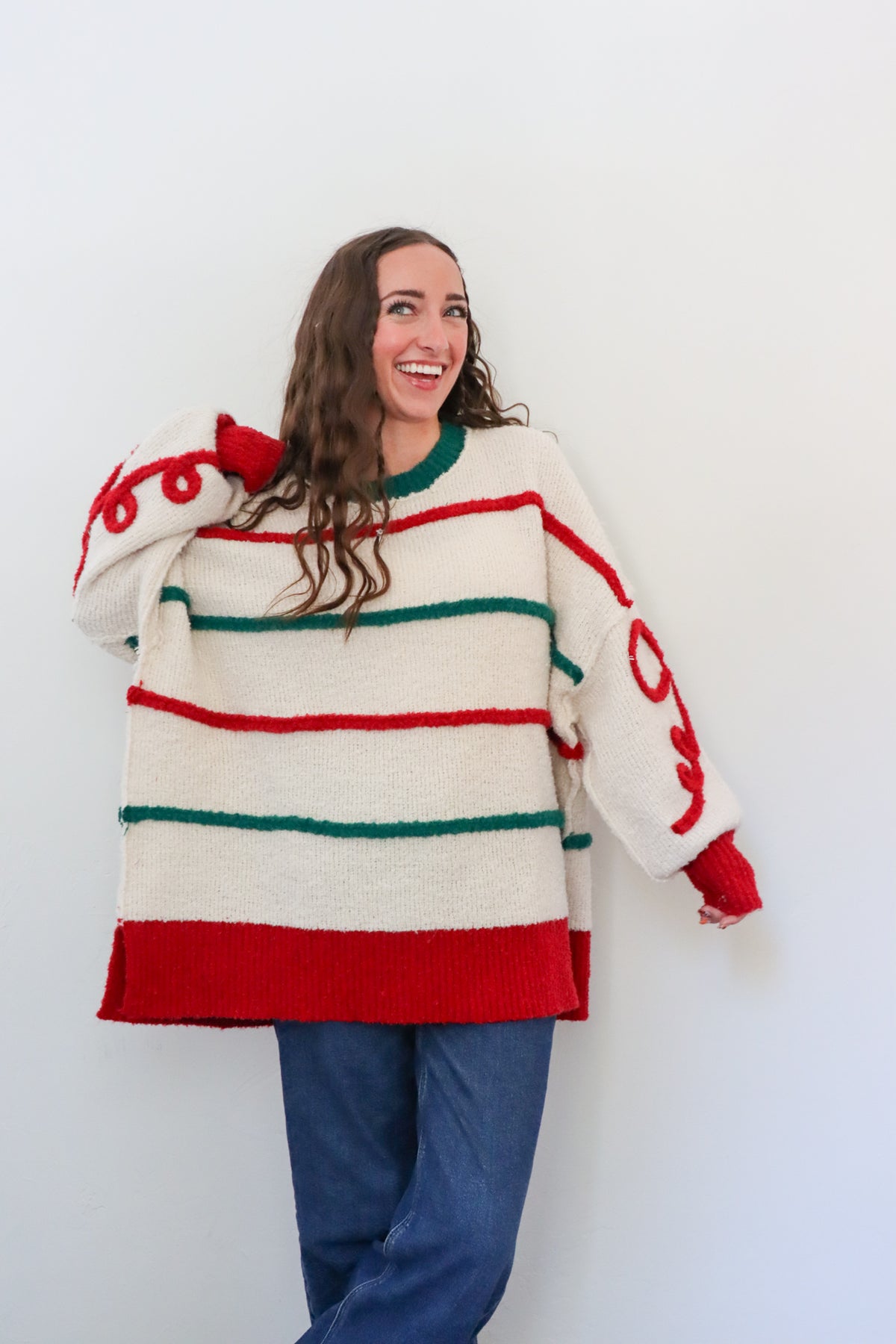 Person wearing a large, colorful sweater with red and green stripes against a white background