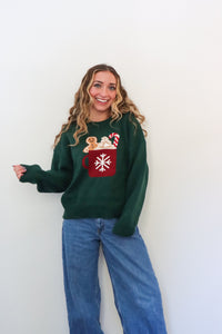 girl wearing dark green knit sweater with hot cocoa graphic