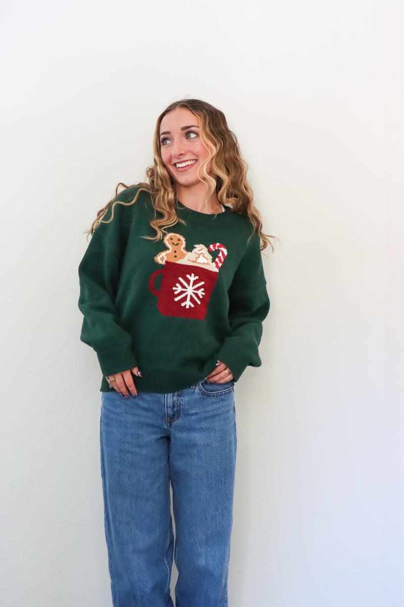 girl wearing dark green knit sweater with hot cocoa graphic
