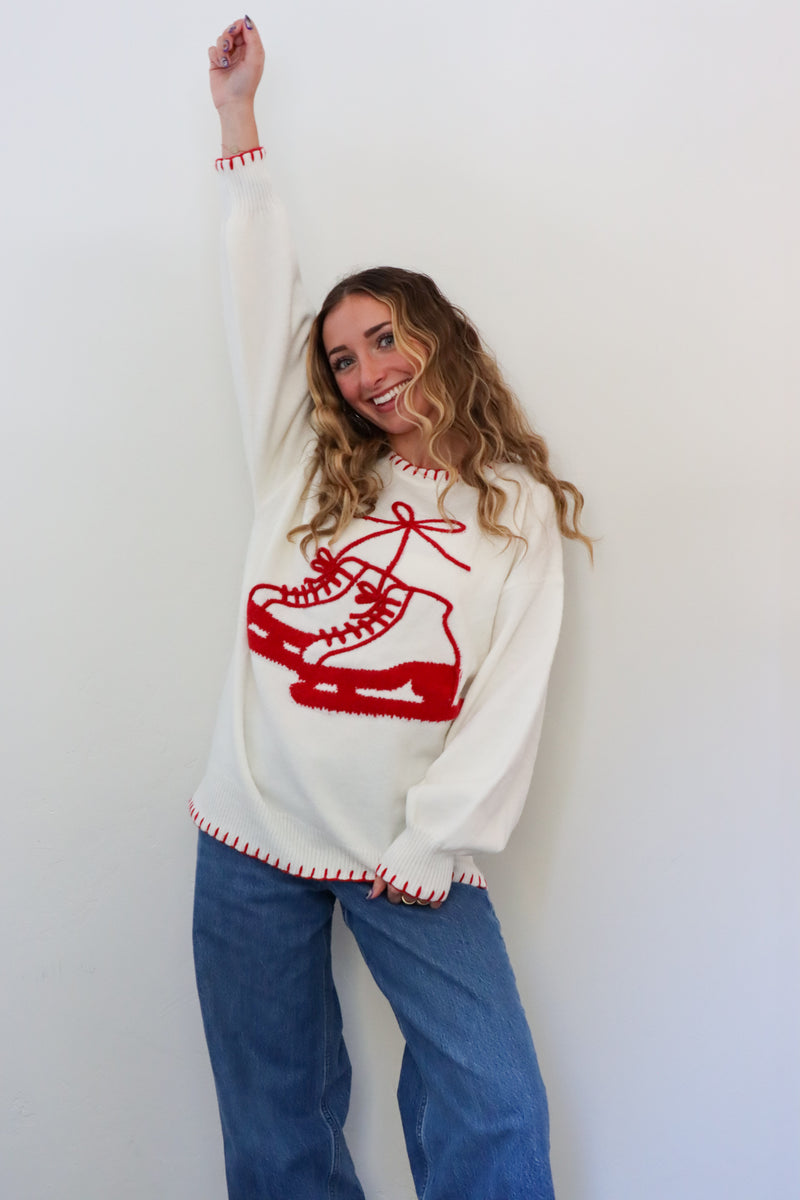 Woman wearing a white sweater with a red ice skate design against a plain background