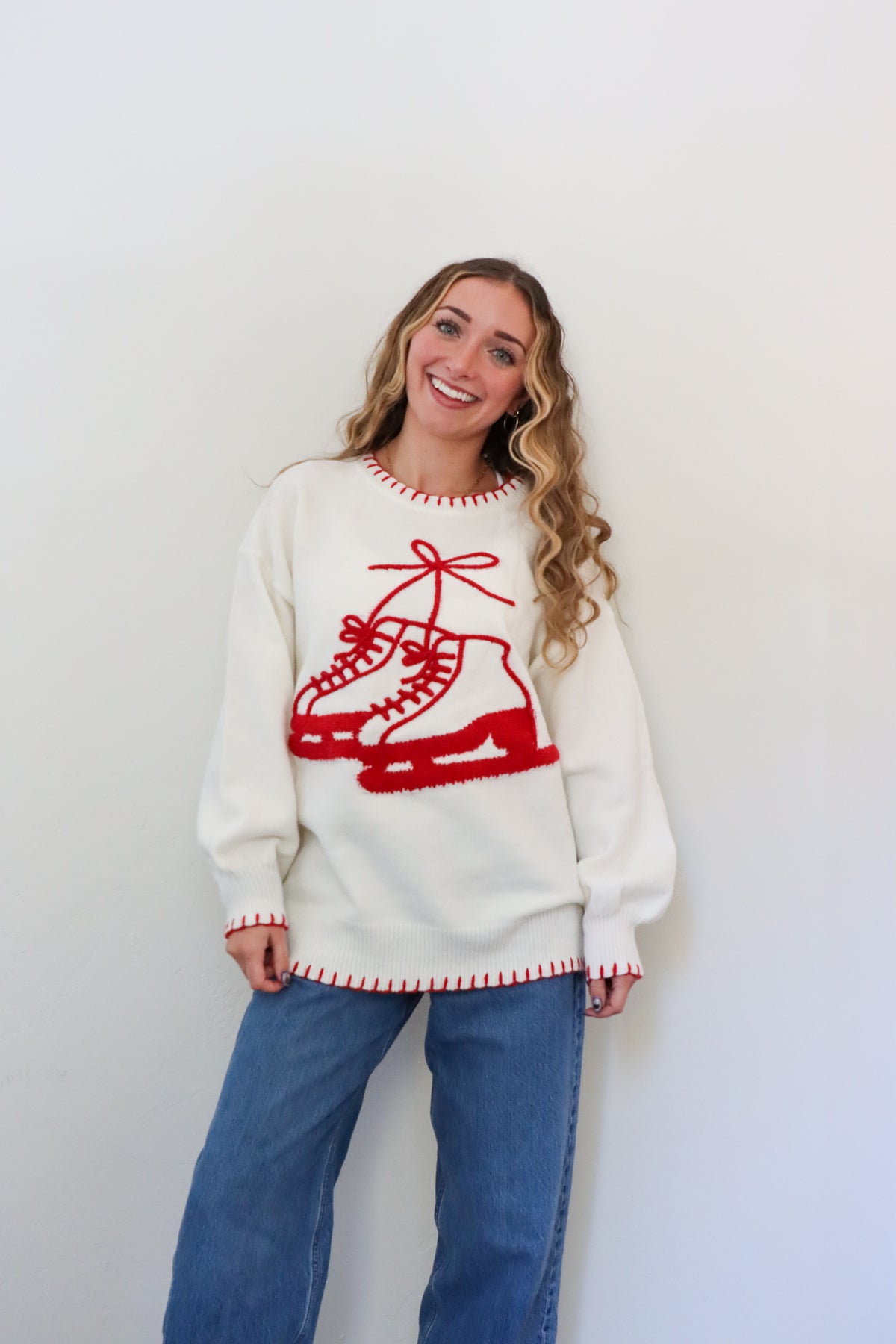 Woman wearing a white sweater with red ice skate design against a plain background