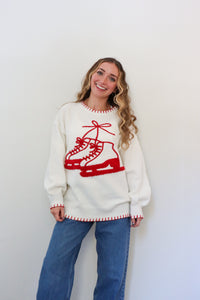 Woman wearing a white sweater with red ice skate design against a plain background
