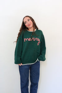 Person wearing a green sweater with 'merry' text against a white background