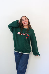 Person wearing a green sweatshirt with 'merry' text against a white background