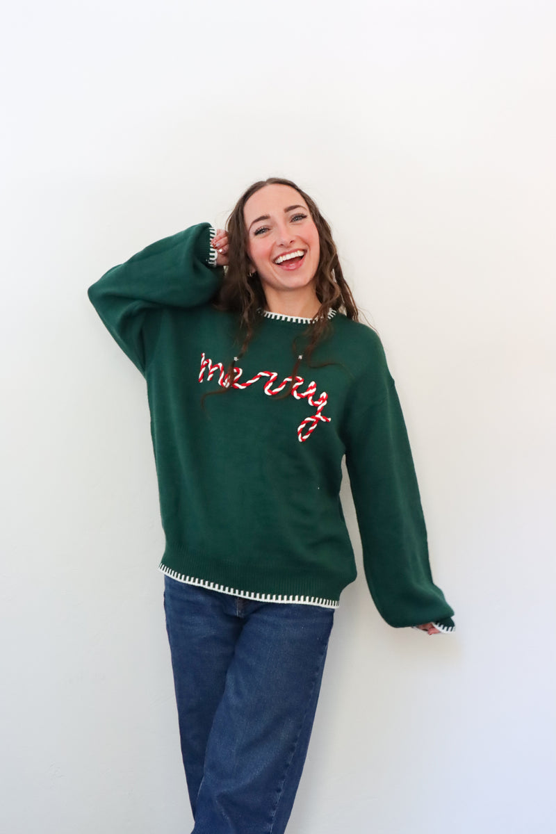 Person wearing a green sweatshirt with 'merry' text against a white background