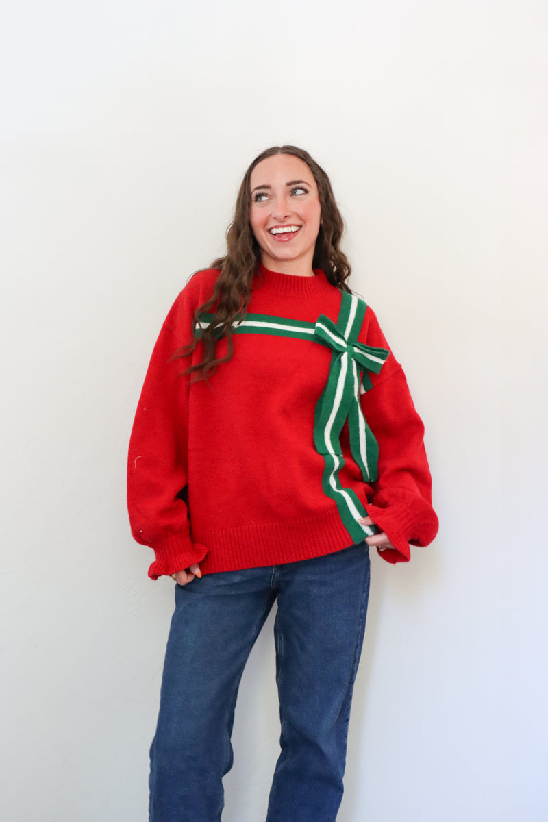 Person wearing a red sweater with a green ribbon design against a white background