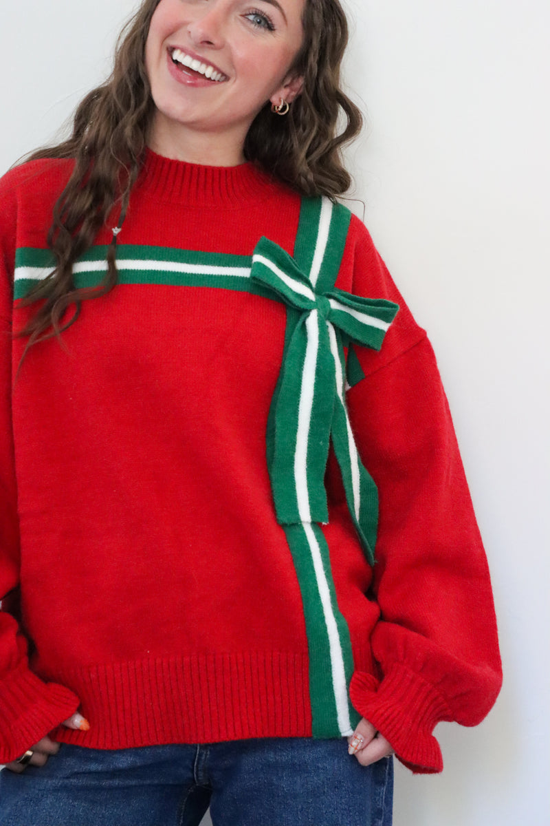 Person wearing a red sweater with a large green bow on a white background