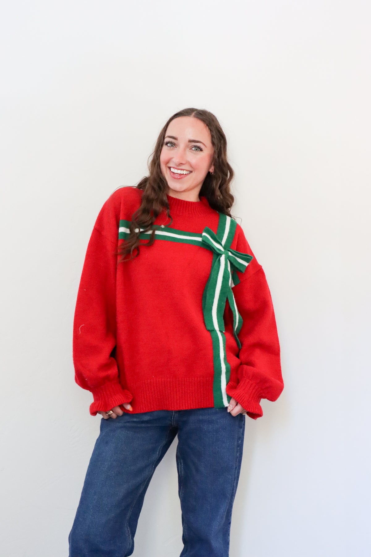 Person wearing a red sweater with a green bow against a white background
