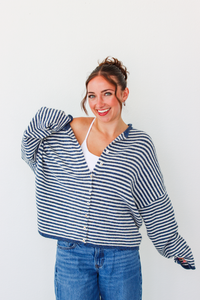 A woman modeling a navy and white striped button-up cardigan over a white tank top and blue jeans, standing against a plain white background.