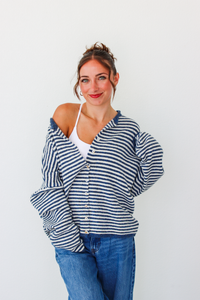 A woman modeling a navy and white striped button-up cardigan over a white tank top and blue jeans, standing against a plain white background.
