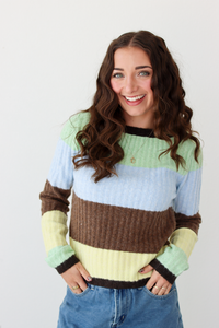 Woman wearing a long sleeve top with brown, green, blue, and yellow stripe and blue denim skirt. 