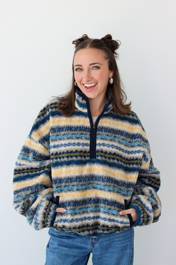 Woman wearing a blue sherpa quarter zip jacket with a pattern and blue denim jeans 