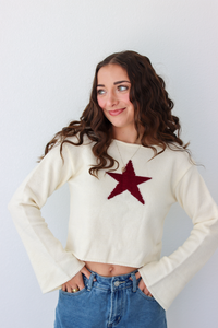 Woman wearing a white knit sweater with a red star graphic in the center and a denim skirt