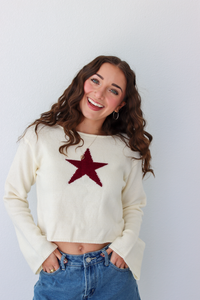 Woman wearing a white knit sweater with a red star graphic in the center and a denim skirt