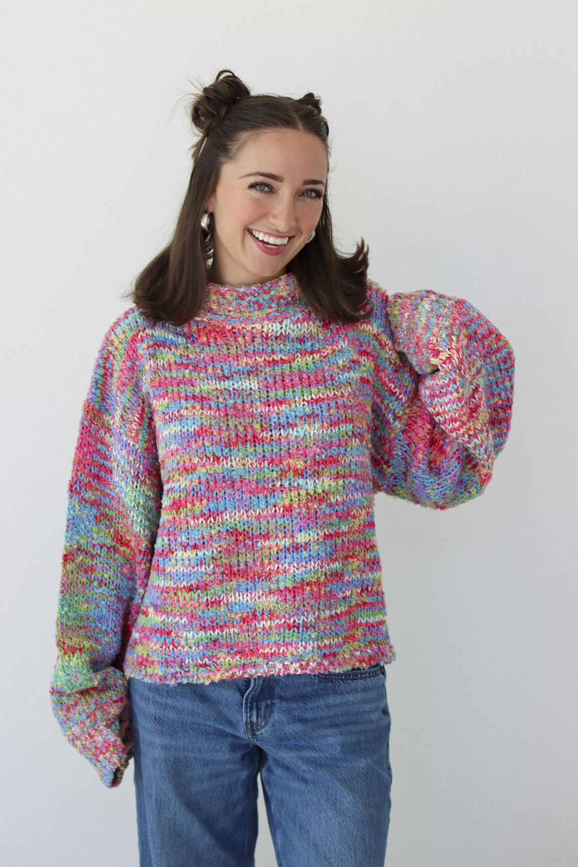 Woman wearing a pink multicolor crochet knit mock neck sweater with blue denim jeans 