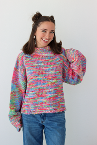 Woman wearing a pink multicolor crochet knit mock neck sweater with blue denim jeans 
