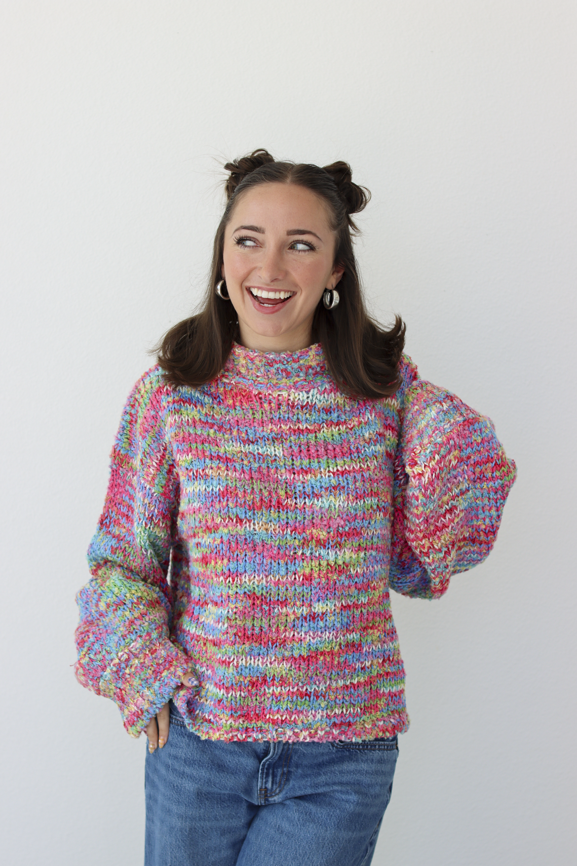 Woman wearing a pink multicolor crochet knit mock neck sweater with blue denim jeans 