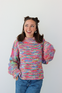 Woman wearing a pink multicolor crochet knit mock neck sweater with blue denim jeans 