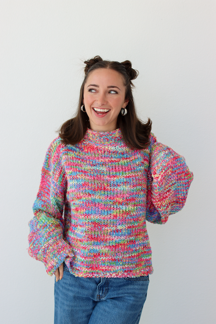 Woman wearing a pink multicolor crochet knit mock neck sweater with blue denim jeans 