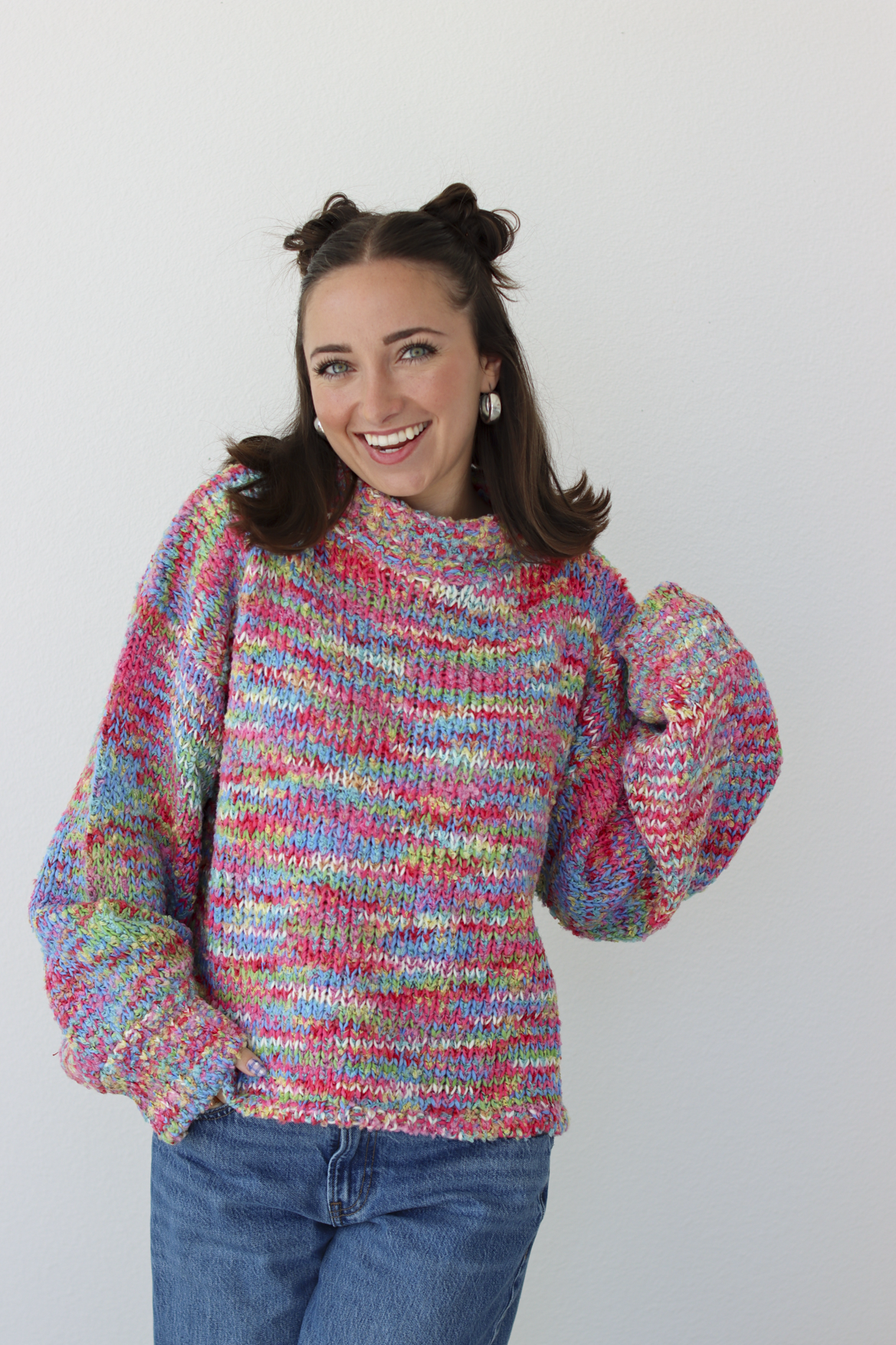 Woman wearing a pink multicolor crochet knit mock neck sweater with blue denim jeans 