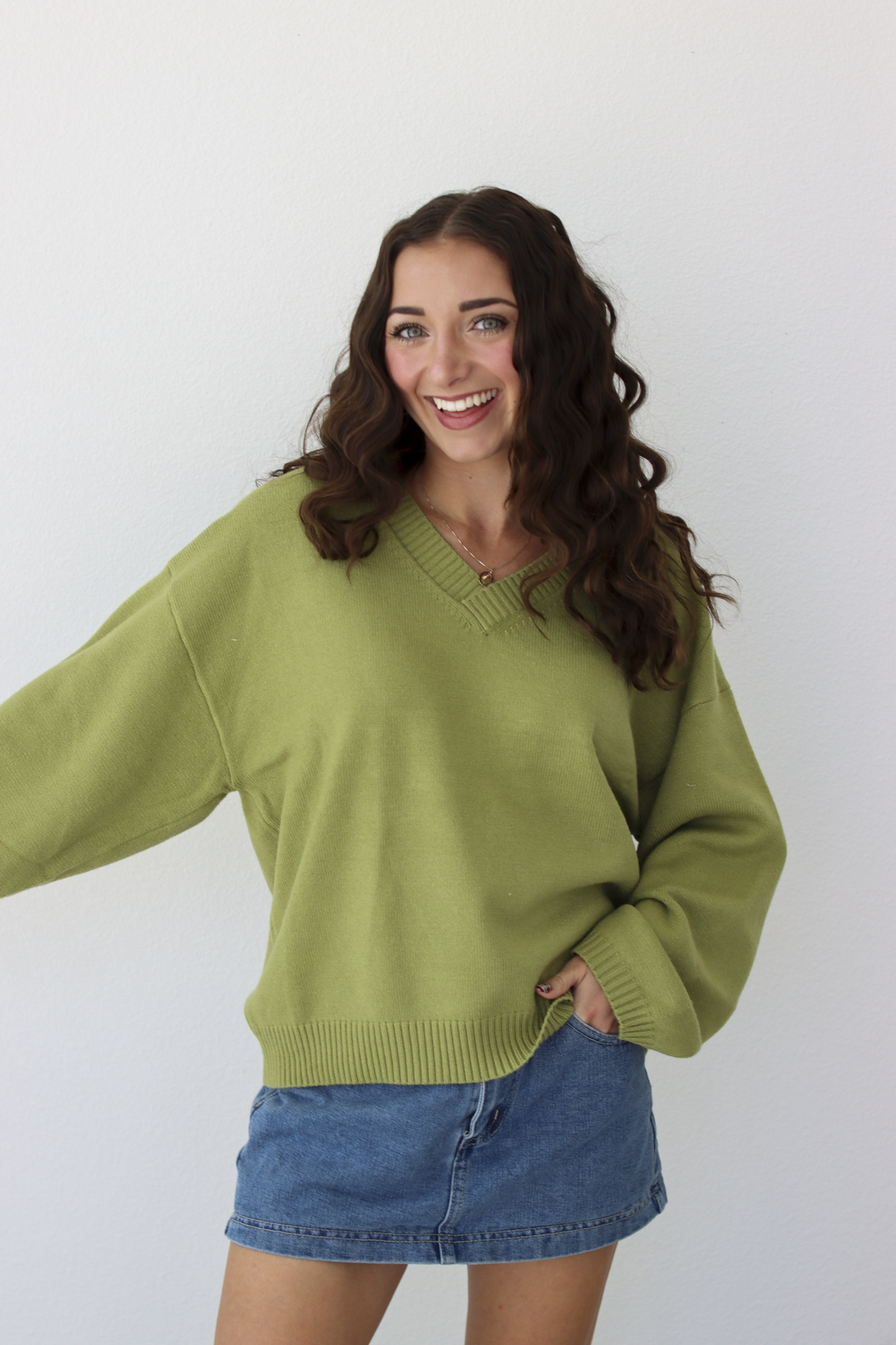 Woman wearing a v-neck green sweater with a blue denim mini skirt 